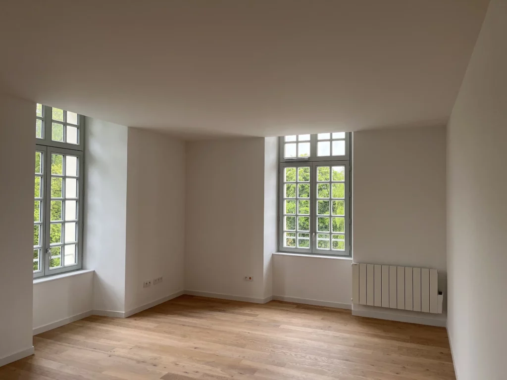 Pièce principale lumineuse avec parquet massif et grandes fenêtres offrant une vue panoramique – appartement Juilly